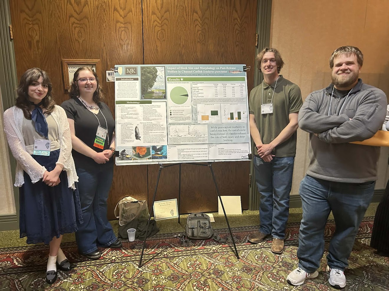 Paisley Gabel, Olivia Miner, Austin Crouse, and Dr. Louison pose for a photo by their poster presentation at the Illinois Chapter of the American Fisheries Society